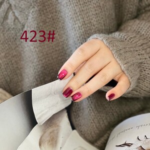 May include: Close-up of a hand with red glitter nail polish. The nails are short and rounded. The hand is wearing a brown sweater. The image is labeled "423#"