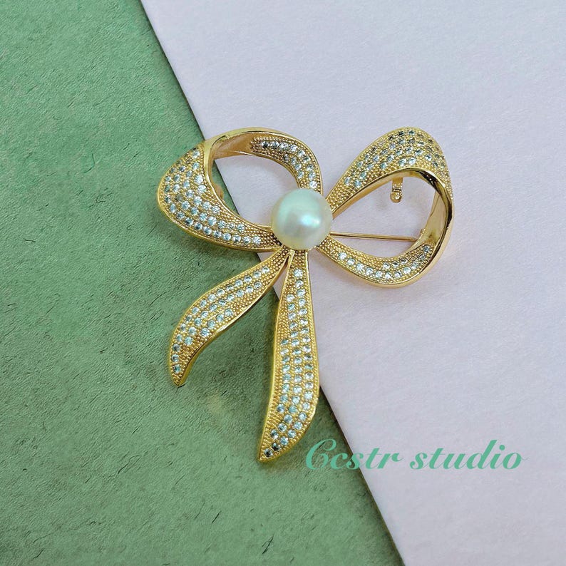 May include: A gold-tone bow brooch with clear rhinestones and a single white pearl in the center.