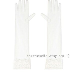 May include: A pair of sheer white opera-length gloves featuring a delicate scalloped lace trim at the wrist. The gloves are translucent and extend to the forearm. The text ccstrstudio. etsy. com :) is printed in black between the two gloves.
