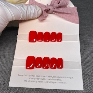 May include: Two rows of ten red press-on nails on a white card. The card has text that reads: "Every Press-on nail has its own chaim, tellingyou are unique. Change as you like, switch quickly, and let beauty never stop with press-on nails."