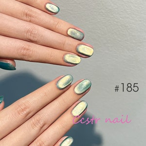 May include: Close-up of fingernails with a light green and gold iridescent shimmer nail polish. The nails are short and oval shaped. The text #185 and ccstrnail is visible in the image.