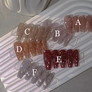 Puede incluir: Seis filas de puntas de uñas con purpurina en varios colores, incluyendo plata, rosa y rojo. Las puntas están etiquetadas con las letras de la A a la F.