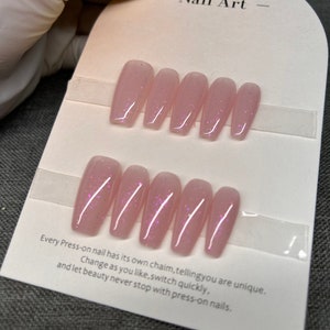 Könnte beinhalten: Ein Set mit zehn pinkfarbenen Press-on-Nägeln mit Glitzer. Die Nägel sind in zwei Reihen zu fünf auf einer weißen Karte angeordnet, auf der der Text "Art" und "Every Press-on nail has its own chaim, tellingyou are unique. Change as you like, switch quickly, and let beauty never stop with press-on nails." steht.