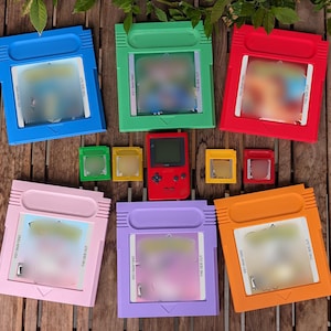May include: A collection of six large colorful plastic game cartridges in blue, green, red, pink, purple, and orange, alongside four smaller matching cartridges and a central red handheld video game console with a screen and directional buttons.