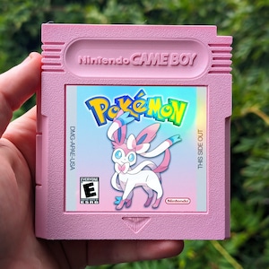 Op de afbeelding: Een roze Nintendo Game Boy-cartridge met het Pokémon-spel. De cartridge heeft het Pokémon-logo en een Sylveon-karakterillustratie. De cartridge heeft ook de ESRB-classificatie en de tekst "THIS SIDE OUT".