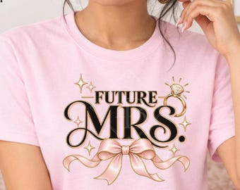 May include: A light pink short-sleeve t-shirt featuring the text FUTURE MRS in black lettering, a graphic of a diamond ring, and a pink ribbon illustration. The shirt is displayed as a front view mockup with text overlays describing the product.