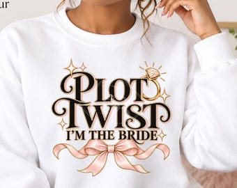 May include: A white crewneck sweatshirt featuring a graphic print with the text Plot Twist I'm The Bride in black lettering, accompanied by a gold diamond ring illustration and a light pink ribbon bow design centered on the chest area.