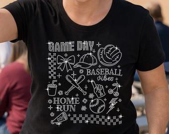 以下が含まれることがあります： 野球をテーマにしたデザインの黒いTシャツ。「Game Day」と「Baseball Vibes」の文字と、グローブ、バット、ボールなどの野球関連のグラフィックが特徴です。デザインは、小さくキラキラ光る装飾で作られています。