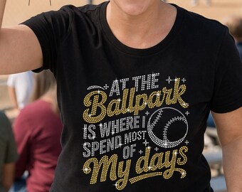 以下が含まれることがあります： 「At the Ballpark is Where I Spend Most of My Days」の文字がラインストーンでデザインされた黒いTシャツ。野球のグラフィックが特徴で、野球の試合で人が着ています。