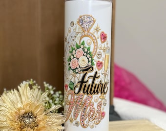 May include: A white cylindrical tumbler with a clear straw featuring a graphic print of a diamond ring, a bouquet of pink and white roses, and a champagne flute. The text "Future Mrs" is written in black and pink script with rhinestone accents.
