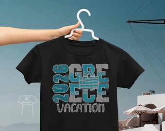 以下が含まれることがあります： ラインストーンのデザインで「2026 GREECE VACATION」と書かれた黒いTシャツ。「GREECE」の文字は青と白の模様です。白いハンガーにかけられたシャツ。
