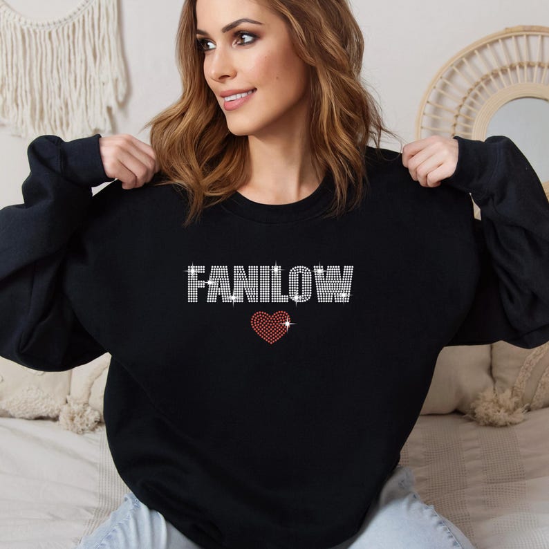 K&ouml;nnte beinhalten: Schwarzes Sweatshirt mit dem Wort "FANILOW" in Strassbuchstaben und einem roten Herz. Das lang&auml;rmlige Oberteil ist ein l&auml;ssiger Stil.