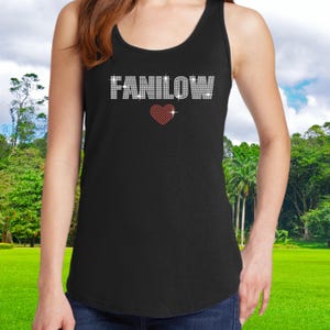 K&ouml;nnte beinhalten: Schwarzes Tanktop mit dem Wort "FANILOW" in Strassbuchstaben und einem roten Strassherz. Das Top ist &auml;rmellos und hat einen Rundhalsausschnitt. Der Hintergrund zeigt eine gr&uuml;ne Wiese mit B&auml;umen und blauem Himmel.