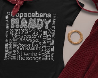 以下が含まれることがあります： Copacabana、Mandy、Ships、could it be magic、Looks like we made it、I write the songs、I made it through the rain、I can't smile without you、Weekend in New Englandというテキストが白いラインストーンで描かれた黒いTシャツ。