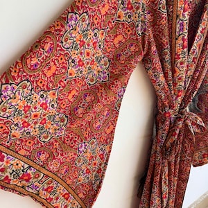 May include: A long red, orange, and brown patterned robe with a floral design. The robe has long sleeves and a tie at the waist.