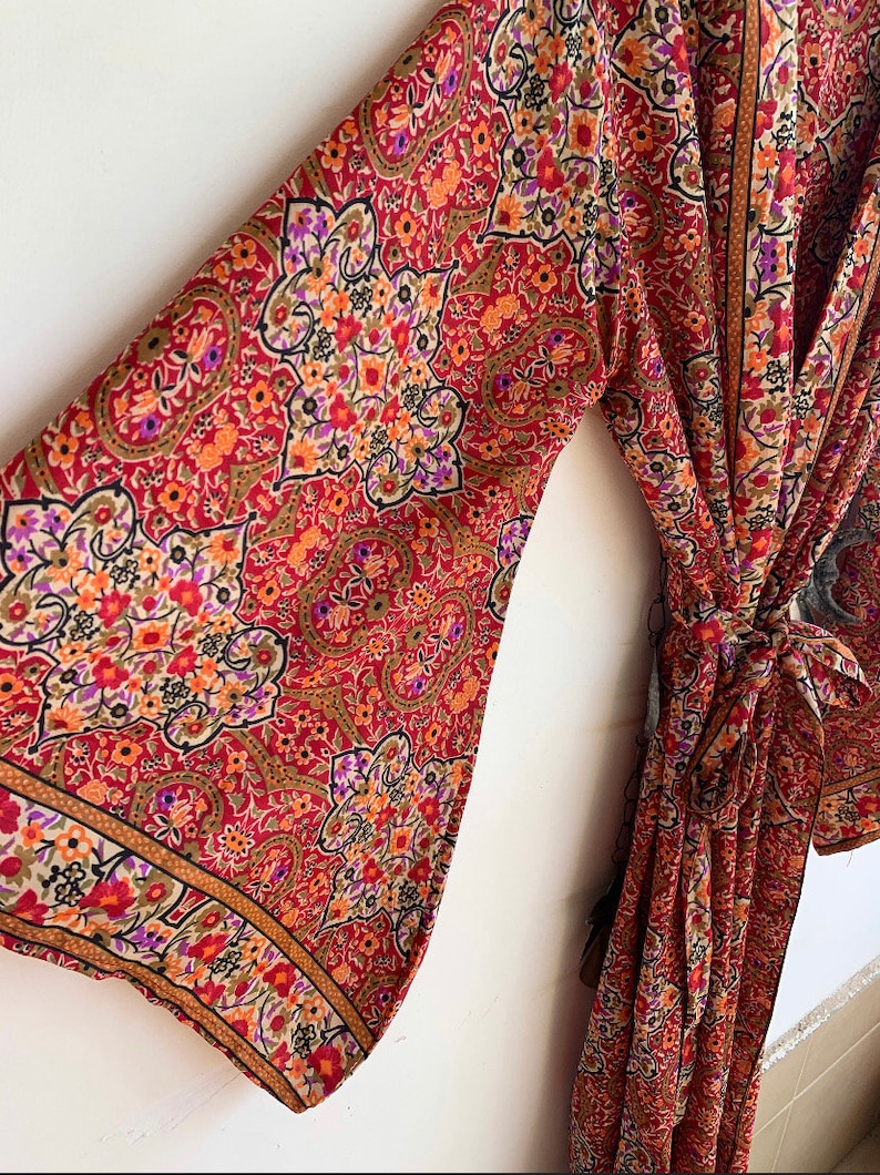 May include: A long red, orange, and brown patterned robe with a floral design. The robe has long sleeves and a tie at the waist.