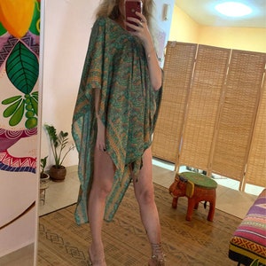 May include: A green and orange patterned kaftan with a V-neck. The lightweight garment is knee-length and has a loose, flowing design. The kaftan is worn with clear high-heeled sandals.