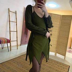Può includere: Un vestito verde con un cardigan a maniche lunghe. Il vestito ha una scollatura a V e una gonna a fessura. Il cardigan ha maniche lunghe e una vestibilità rilassata.