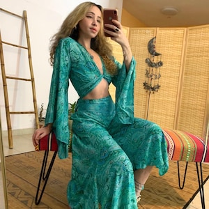 Op de afbeelding: Een tealblauwe twee-delige outfit met een paisley print. Het topje is een crop top met lange mouwen en een twist detail aan de voorkant. De broek is wijd uitlopend en heeft een vloeiende silhouet.