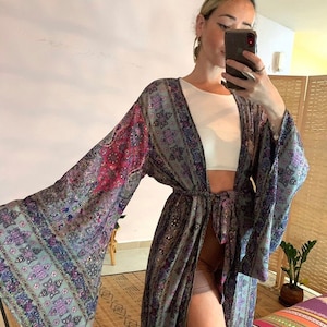 May include: A long, flowing, gray and purple patterned robe with a tie belt. The robe has a V-neck and long sleeves with wide bell bottoms. The robe is made of a soft, silky fabric.