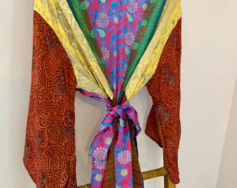 May include: A colorful kimono-style robe with long sleeves, hanging on a wooden rack. The robe features a mix of patterns and colors, including red paisley, pink floral, and yellow and green stripes. The robe is tied at the waist with a matching sash.