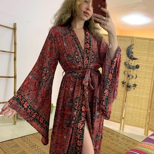 Può includere: Un lungo kimono rosso e nero con stampa paisley, una cintura nera e ampie maniche a campana. Il kimono ha una profonda scollatura a V e uno spacco laterale.