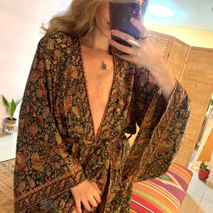 May include: A long, flowing green and gold paisley patterned robe with a deep V-neckline and long sleeves. The robe is tied at the waist with a matching sash.
