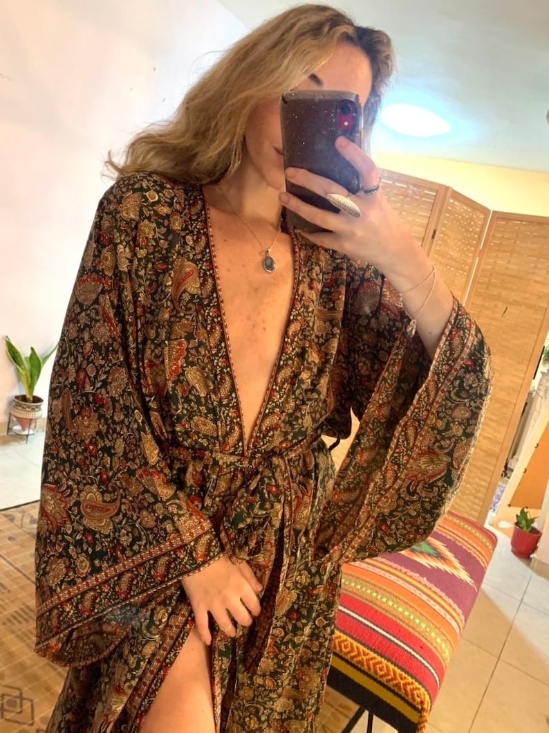 May include: A long, flowing green and gold paisley patterned robe with a deep V-neckline and long sleeves. The robe is tied at the waist with a matching sash.