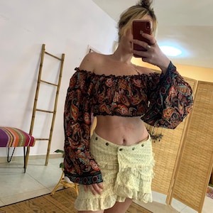 Może przedstawiać: Kobieta w czarno-czerwonej bluzie z dekoltem typu hiszpański w paisley z długimi rękawami i białej mini spódnicy zrobionej na szydełku.