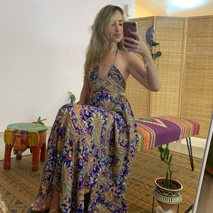 Może przedstawiać: Kobieta w niebiesko-pomarańczowej długiej sukience w paisley z dekoltem halter. Siedzi na ławce z rośliną w doniczce obok niej.