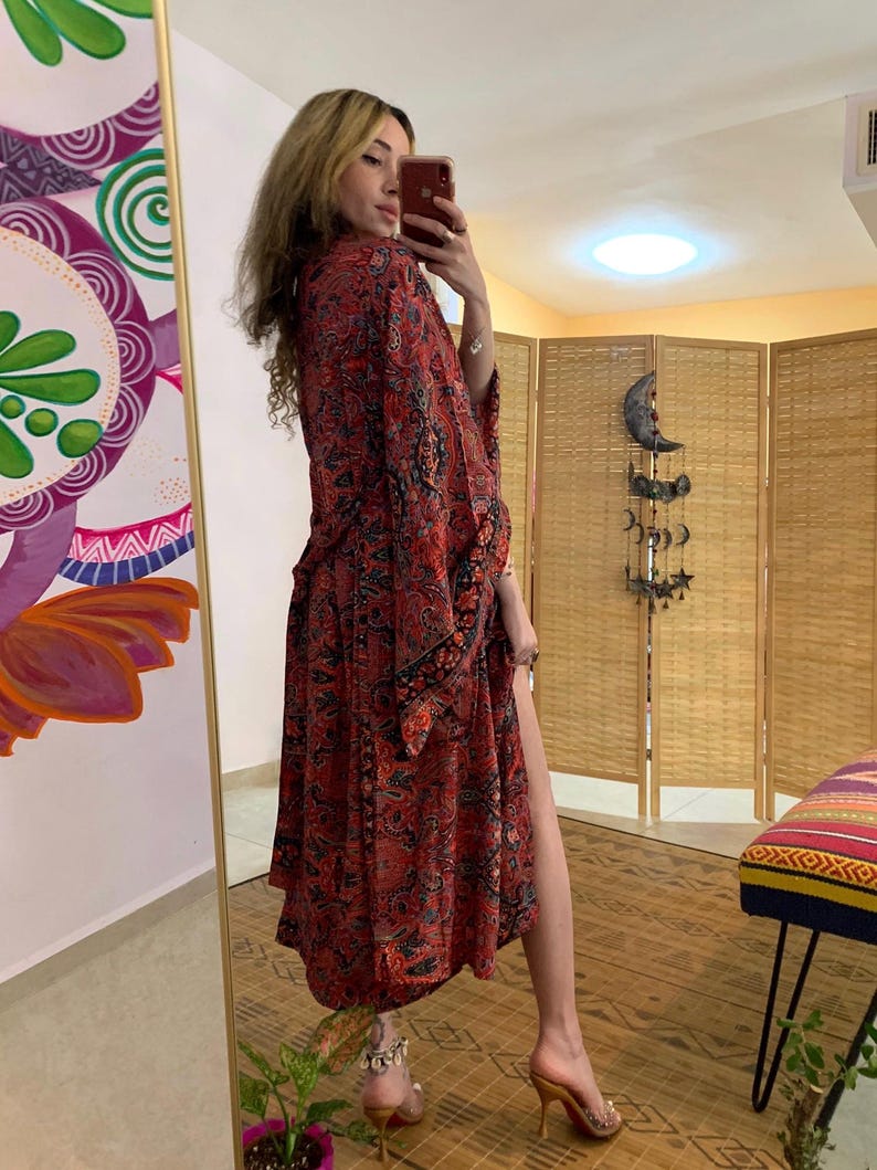 May include: A long, flowing red kimono-style robe with a paisley pattern in black and other colors. The robe is open in the front and has long sleeves. The person in the image is wearing high-heeled shoes.