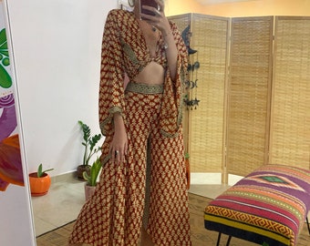 Puede incluir: Un conjunto de dos piezas con estampado rojo y dorado, con un top corto y pantalones de pierna ancha. El top tiene un detalle anudado en la parte delantera y los pantalones tienen una pierna ancha y un dobladillo dividido.