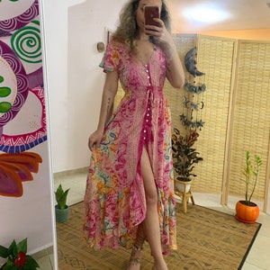 Op de afbeelding: Een roze maxi-jurk met een bloemenprint en een knoopsluiting aan de voorkant. De jurk heeft een hoge split en een gerimpelde zoom.