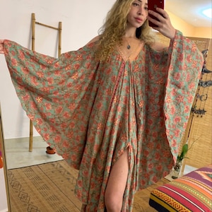 Peut inclure: Longue robe fluide à manches larges, ornée d'un motif floral vert et corail. La robe présente une encolure en V et une fente haute. Le tissu léger suggère une tenue d'été. Le style rappelle un caftan.