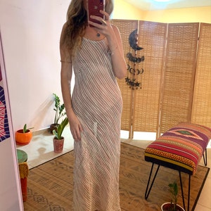 Pode incluir: Um vestido maxi branco com finas listras rosa e marrom. O vestido tem um decote redondo e um caimento solto.