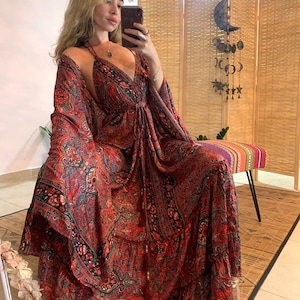 Könnte beinhalten: Ein langes, fließendes Maxikleid mit Paisley-Muster in Rot und Schwarz mit einer passenden Jacke im Kimono-Stil. Das Kleid hat einen tiefen V-Ausschnitt und eine Binde in der Taille.