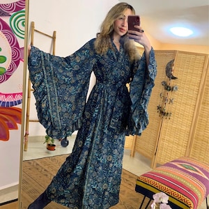 Könnte beinhalten: Langes, fließendes, marineblaues Kleid mit floralem Muster. Das Kleid hat weite, gerüschte Ärmel und einen passenden Gürtel. Der Stoff hat einen subtilen Glanz. Geeignet zum Entspannen oder als stilvoller Überwurf.