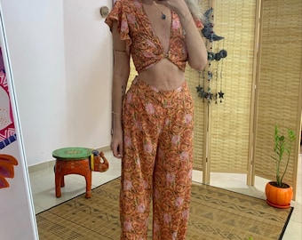May include: A two-piece outfit with a floral print in shades of orange, pink, and green. The top is a crop top with a knotted front and short, ruffled sleeves. The pants are wide-legged and flowy.