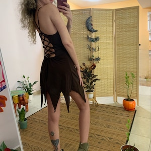 Könnte beinhalten: Ein braunes Minikleid mit Schnürung im Rücken. Das Kleid hat einen fließenden Rock mit spitzem Saum. Das Model trägt das Kleid mit grünen Stiefeletten.