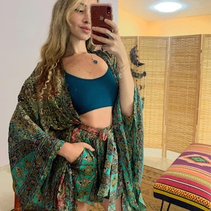 Può includere: Una donna indossa un kimono verde e oro con un top a fascia turchese e pantaloncini abbinati verde e oro.