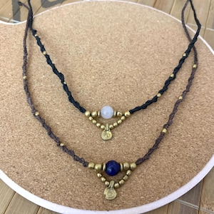 May include: Two layered necklaces with black and brown cords, gold beads, and a white and blue stone pendant.