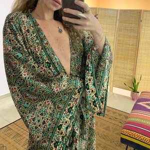 May include: A green and brown patterned long-sleeved dress with a deep V-neckline. The dress has a floral and paisley design with a green border. The dress is worn by a person with long brown hair.