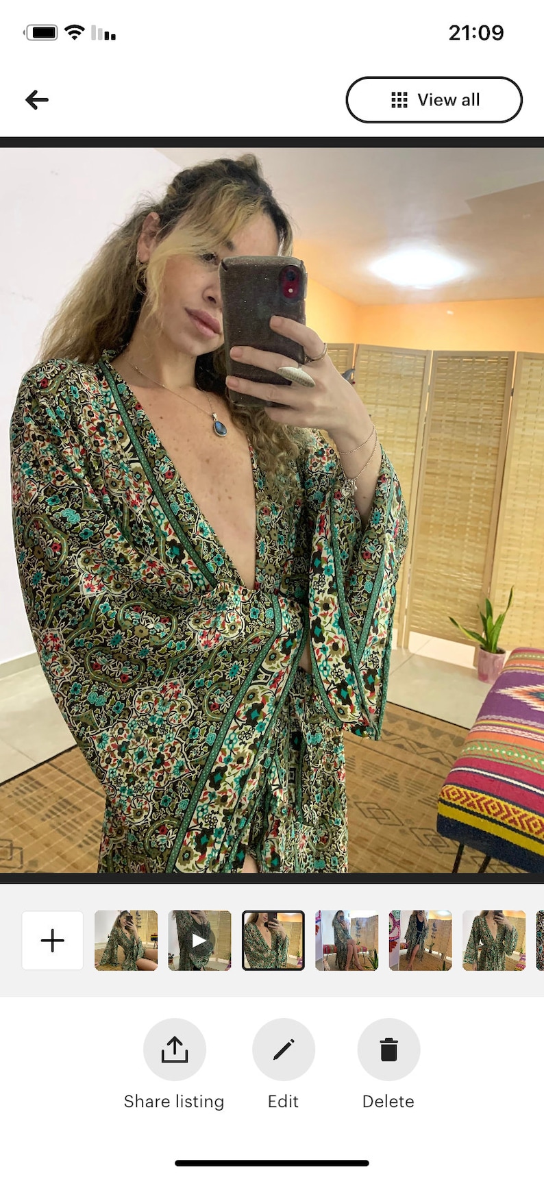 May include: A green and brown patterned long-sleeved dress with a deep V-neckline. The dress has a floral and paisley design with a green border. The dress is worn by a person with long brown hair.
