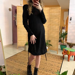 May include: A black long-sleeved dress with ruched sleeves and a drawstring hem. The dress is paired with black combat boots. The person is holding a phone in front of a mirror.