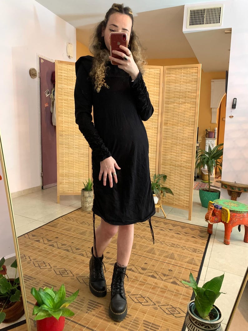 May include: A black long-sleeved dress with ruched sleeves and a drawstring hem. The dress is paired with black combat boots. The person is holding a phone in front of a mirror.