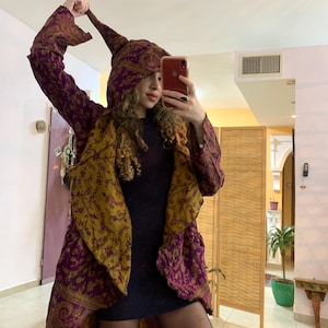 May include: A long, purple and gold patterned hooded jacket with a flowing design. The jacket has a paisley print and is made of a soft, flowing fabric.