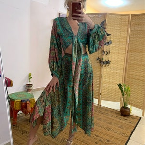Op de afbeelding: Een turquoise tweedelige outfit met een bloemenpatroon. De top heeft lange mouwen en een striksluiting. De rok is lang en vloeiend. De outfit is gemaakt van een lichte stof. Geschikt voor een bohemien- of resortstijl.