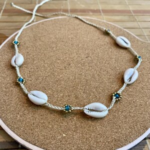 May include: A white shell necklace with blue and gold beads. The necklace is made of a natural material and has a simple design.