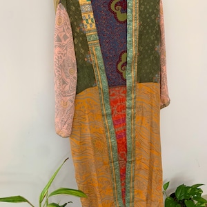 May include: A long-sleeved duster robe featuring a patchwork design of various fabrics. The garment displays an olive green upper section, a bright orange lower section with floral patterns, and light pink sleeves with geometric prints.