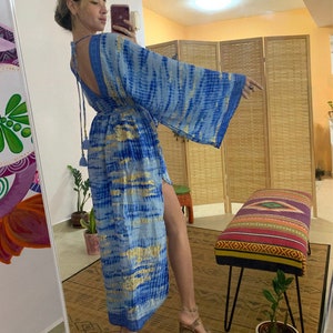 May include: A long, blue and gold tie-dye maxi dress with a deep V-neck and long sleeves. The dress has a tassel detail at the waist.